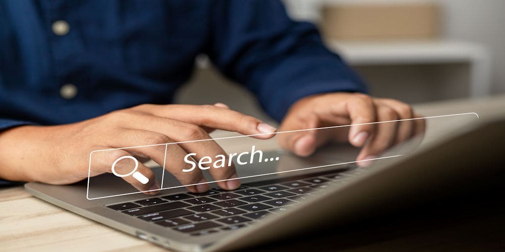 Close-up of hands typing on a laptop with a translucent search bar reading 'Search...' overlaying the keyboard